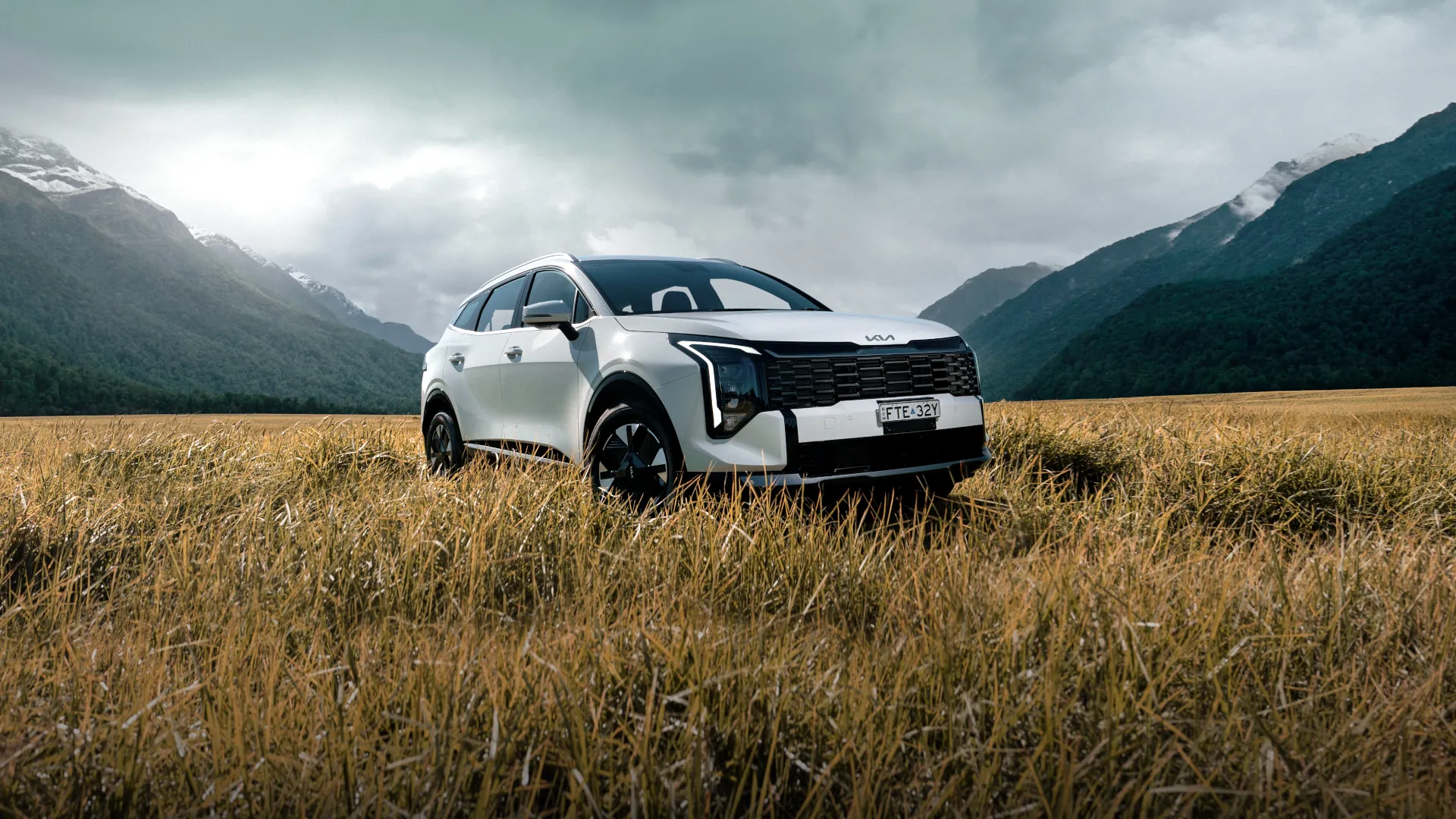 White Kia Sportage Hybrid in a mountain landscape — manufacturer campaign artwork