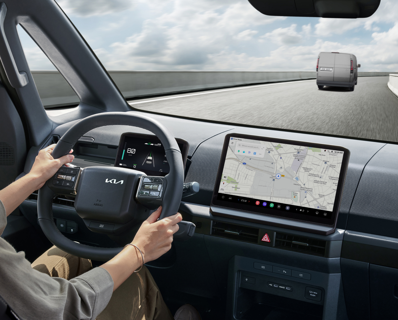 Driver holding steering wheel of the Kia PV5 Cargo with navigation screen visible
